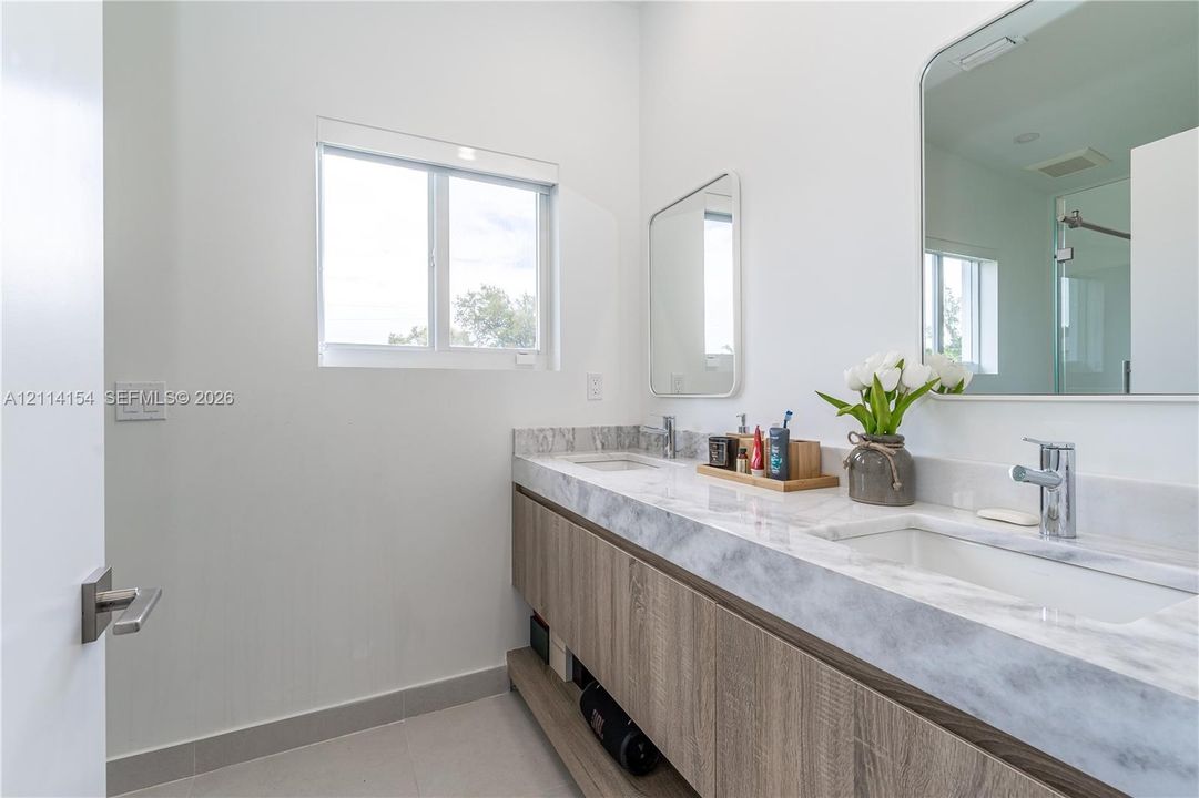 Dual-sink floating vanity with wood-finish cabinetry, stone-style countertop, rectangular undermount sinks, and rounded rectangular mirrors