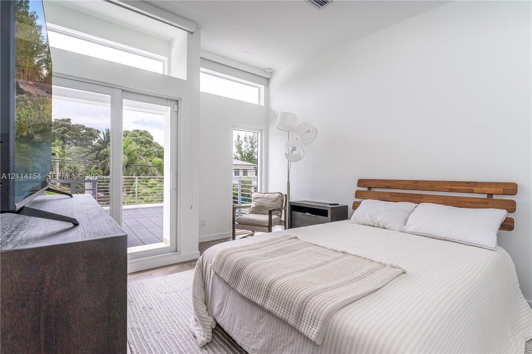 High-ceilinged room featuring expansive clerestory windows, a full-height glass door, and a private balcony with horizontal metal railings