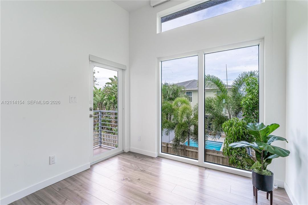 High ceilings featuring expansive picture windows and clerestory glass, wood-finish flooring, and a glass-panel exterior door opening to a balcony
