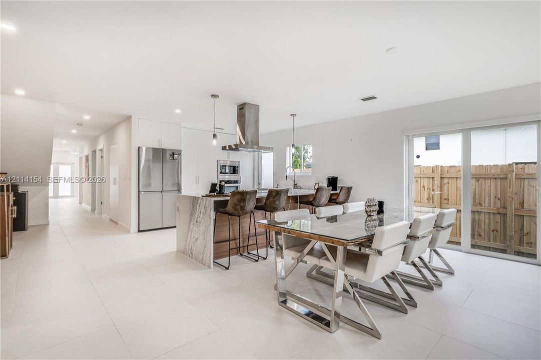 Kitchen featuring a waterfall-edge island, stone-patterned countertop, stainless steel appliances, stainless steel range hood, and large-format tile flooring