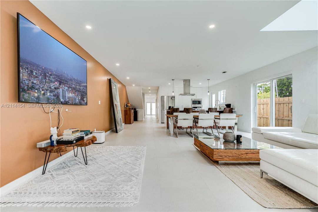 Open-concept interior featuring large-format tile flooring, recessed lighting, a stainless steel kitchen range hood, and sliding glass doors