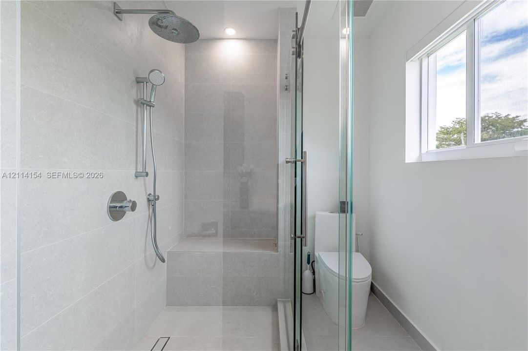 Walk-in shower with light-toned tiled surround, built-in tiled bench, rainfall shower head, adjustable handheld sprayer, and frameless glass enclosure