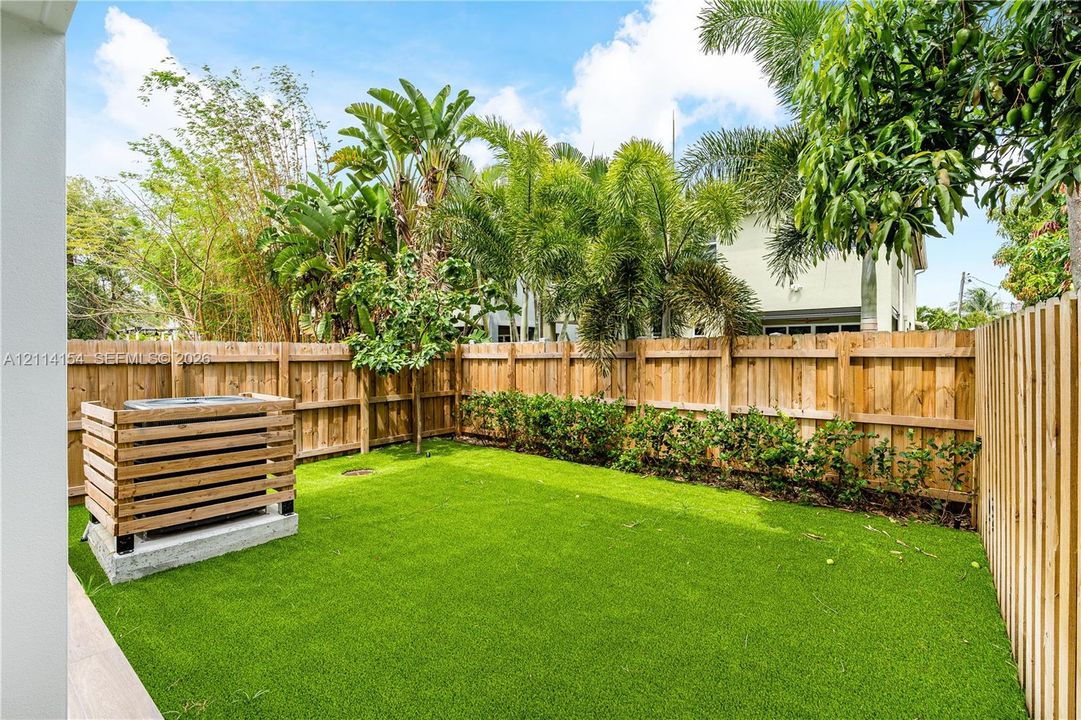 Private backyard featuring synthetic turf, vertical wood privacy fencing, and a built-in wood slat HVAC enclosure