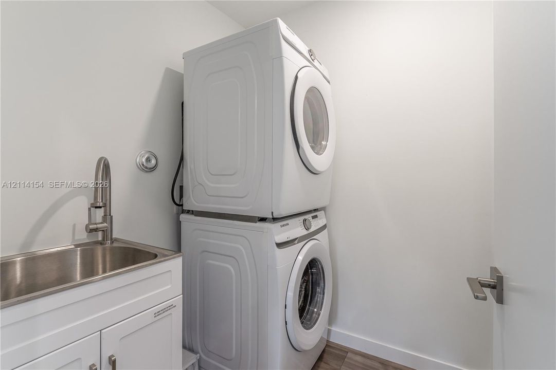 Stacked front-load laundry units with a white finish, stainless steel basin sink, and high-arc brushed nickel faucet set within a white cabinet vanity
