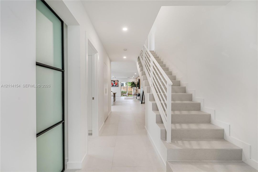 Entryway featuring large-format tile flooring, a staircase with white horizontal railings, recessed lighting, and a frosted glass door with a black frame