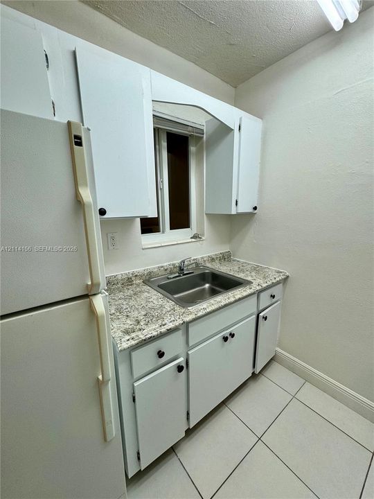 Kitchen featuring white cabinetry, stone-finish countertops, stainless steel sink with metal faucet, and white tile flooring