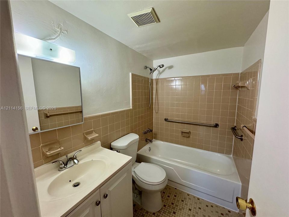 Bathroom featuring a white vanity cabinet with an integrated sink, ceramic tile wainscoting, a bathtub and shower combination, and wall-mounted metal grab bars