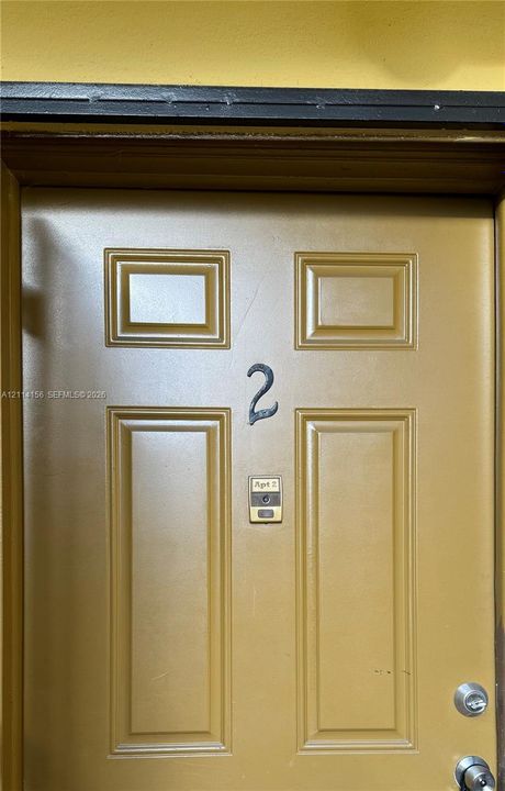 Solid-core four-panel door with a numeric address plaque, integrated electronic doorbell, and dual-lock metallic hardware
