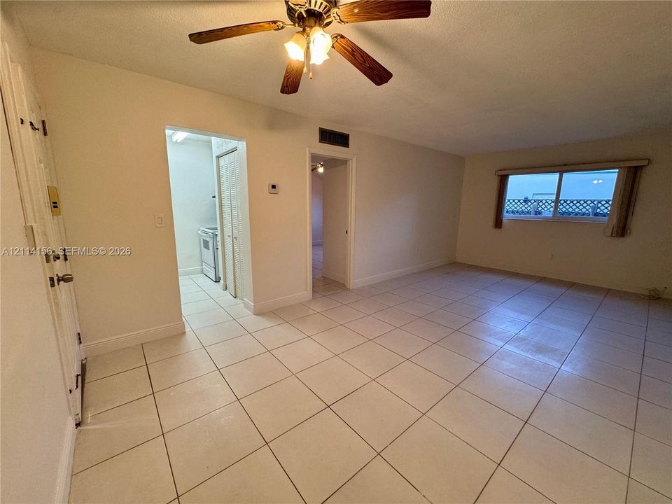 Neutral-toned interior featuring square tile flooring, a multi-blade ceiling fan with integrated lighting, and a large horizontal sliding window