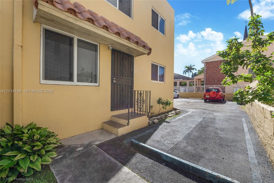 Stucco exterior featuring a decorative tile roof accent, metal security door, and dedicated asphalt parking