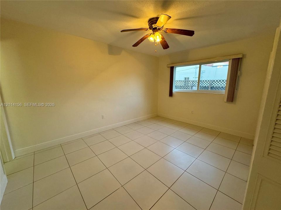 Room featuring light-colored tile flooring, a multi-blade ceiling fan with integrated lighting, and a window with horizontal blinds