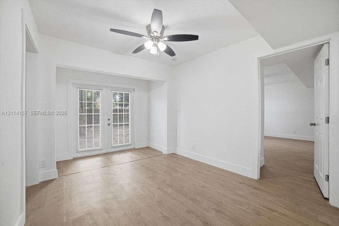 Wood-finish flooring, white paneled interior doors, and glass-paned French doors with a multi-light design, complemented by a central ceiling fan with integrated lighting