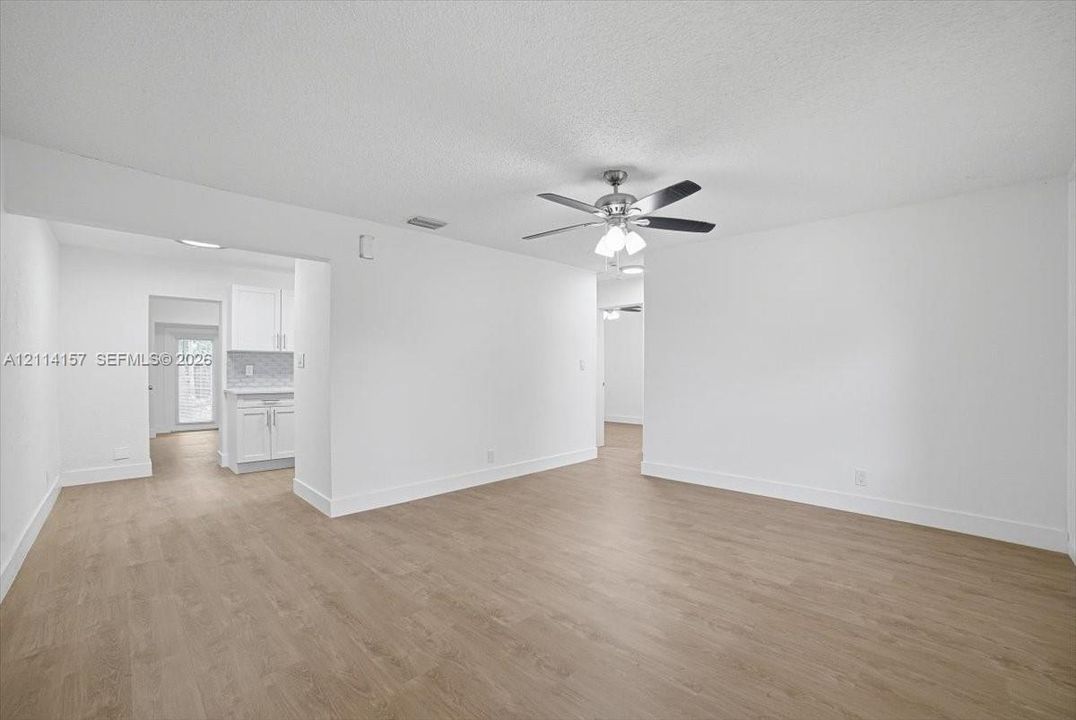 Interior space featuring wood-finish flooring, white walls, and a ceiling-mounted light fixture with a multi-blade fan