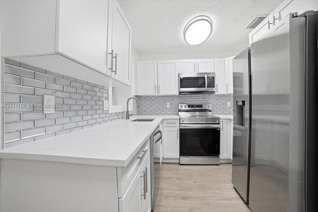 Kitchen featuring white shaker-style cabinetry, white solid-surface countertops, a gray subway tile backsplash, stainless steel appliances, and wood-finish flooring