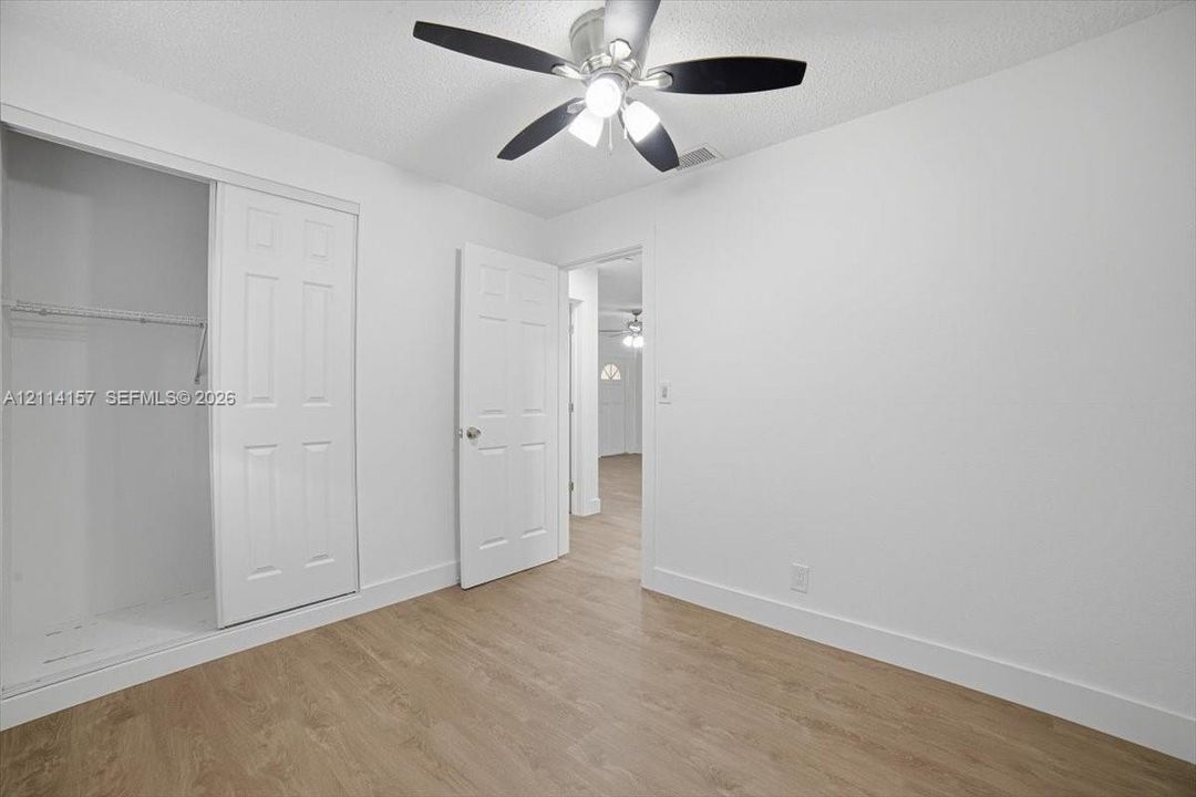Room featuring wood-finish flooring, a ceiling fan with integrated lighting, and a closet with sliding paneled doors