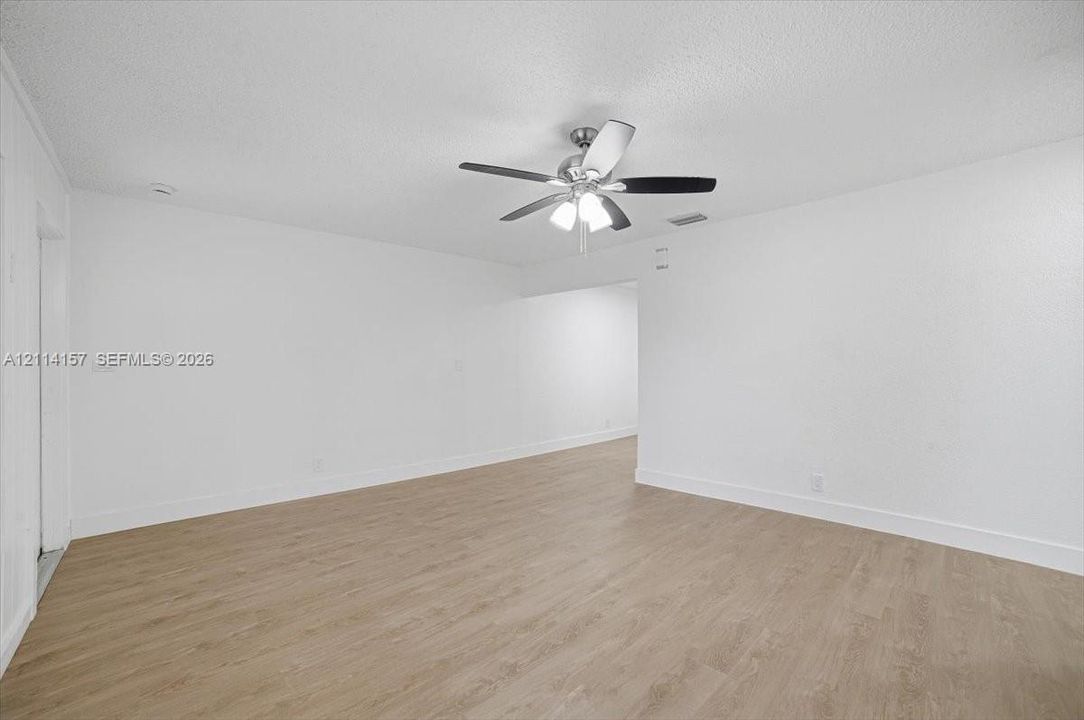 Interior space featuring wood-finish flooring, white walls, and a ceiling fan with integrated lighting