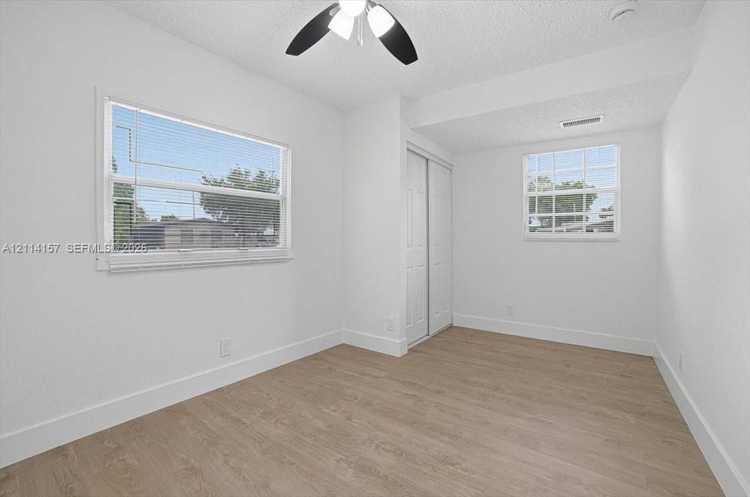 Interior room featuring wood-finish flooring, dual windows with integrated blinds, and a built-in closet with sliding panel doors