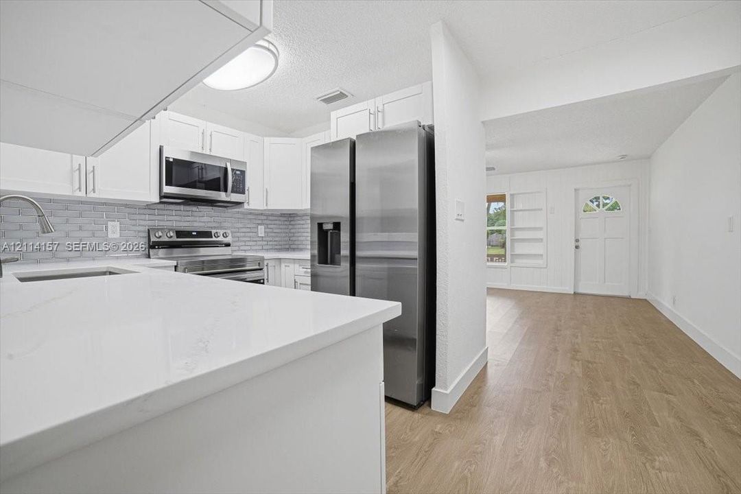 Kitchen featuring white shaker-style cabinetry, solid-surface countertops, a brick-patterned tile backsplash, stainless steel appliances, and wood-finish flooring