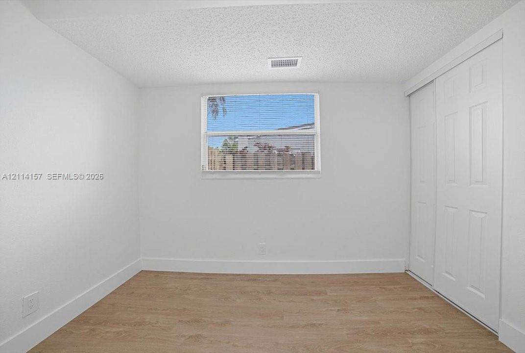 Neutral-toned room featuring wood-finish flooring, a central window with horizontal blinds, and a built-in sliding-door closet