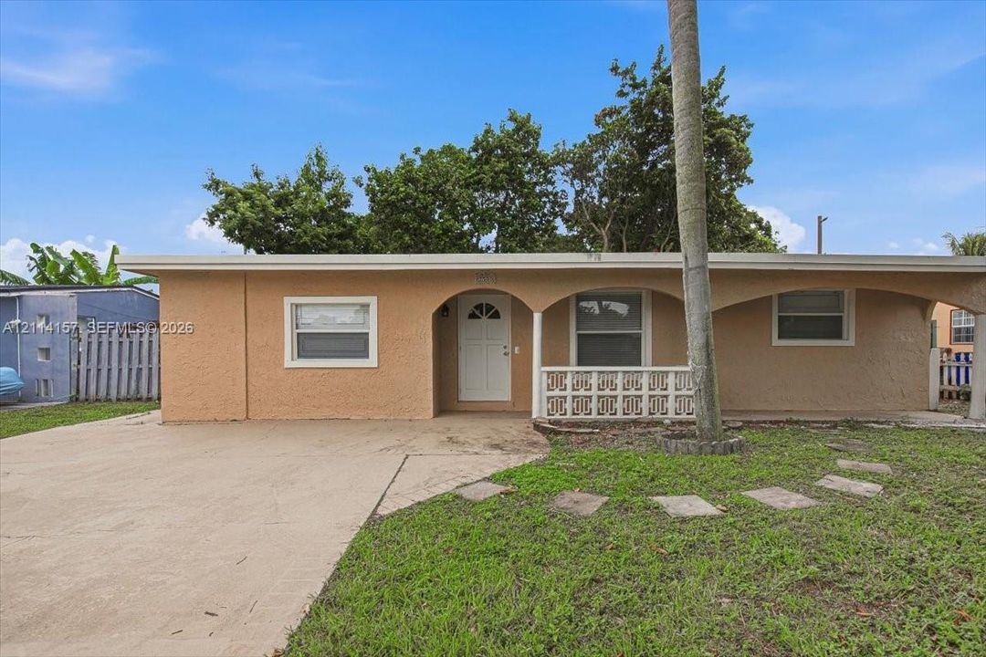 Single-story exterior featuring a stucco facade, covered front porch with arched openings, decorative concrete block screening, and a concrete driveway