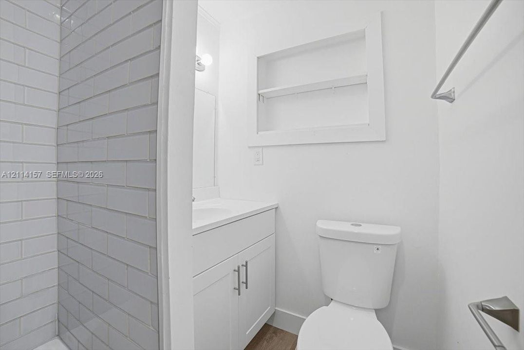 Bathroom featuring subway tile shower surround, white vanity with integrated basin, recessed wall niche, and polished chrome hardware
