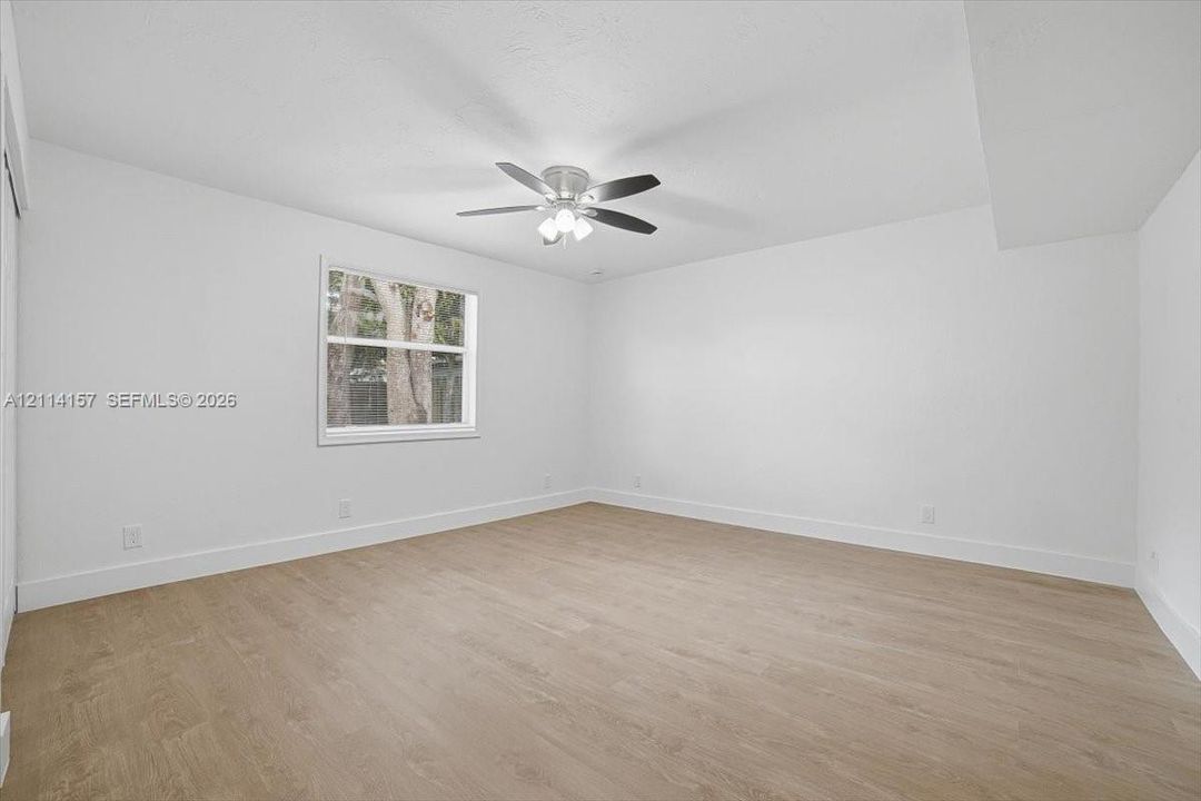 Bright room featuring wood-finish flooring, a neutral color palette, a single-hung window, and a multi-blade ceiling fan with integrated lighting