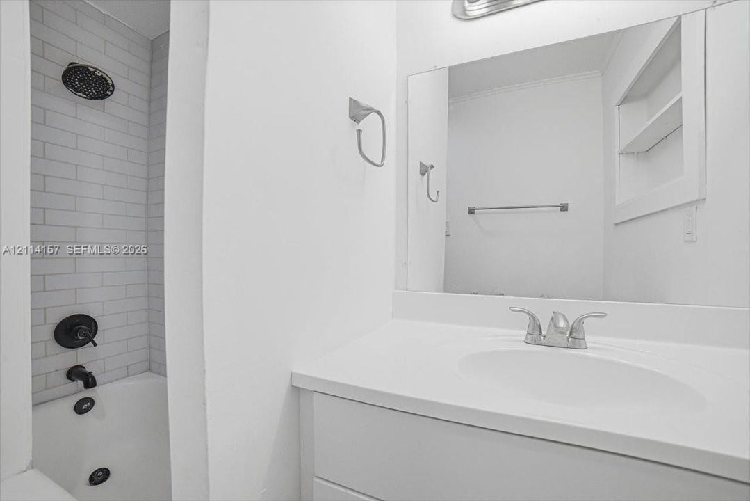Bathroom featuring a white vanity with a composite countertop, subway tile shower surround, matte black shower fixtures, large rectangular vanity mirror, and built-in recessed shelving