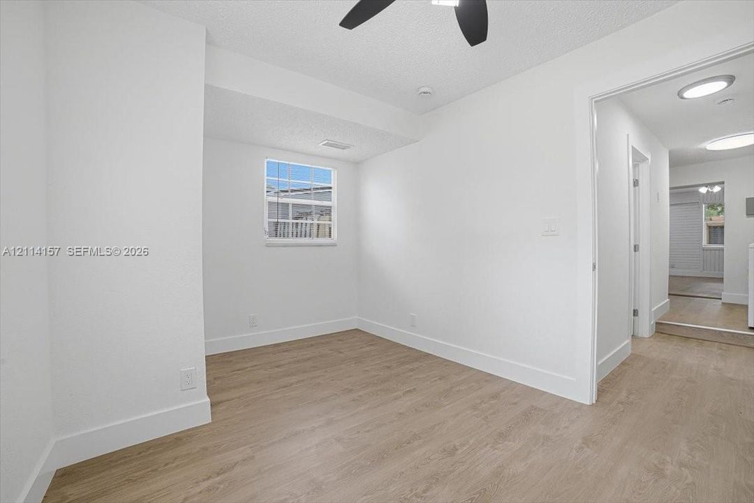 Room featuring wood-finish flooring, a grid-pane window, and a multi-blade ceiling fan