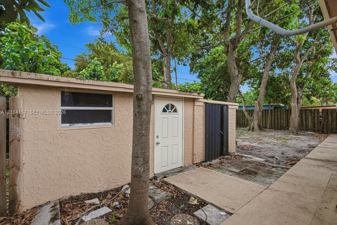 Exterior storage structure featuring a stucco finish, single-entry door with glass detail, horizontal sliding window, and metal privacy screen