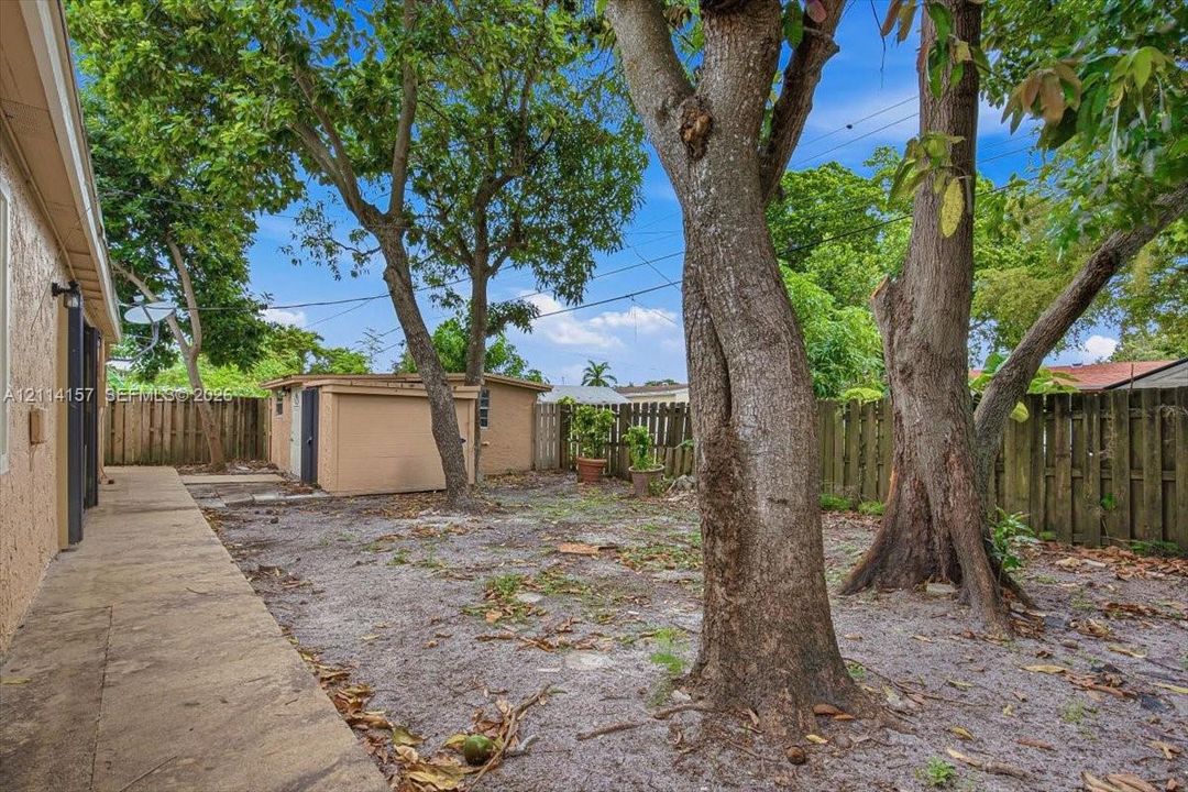 Rear yard featuring a concrete walkway, detached storage structure, and wood privacy fencing with mature trees
