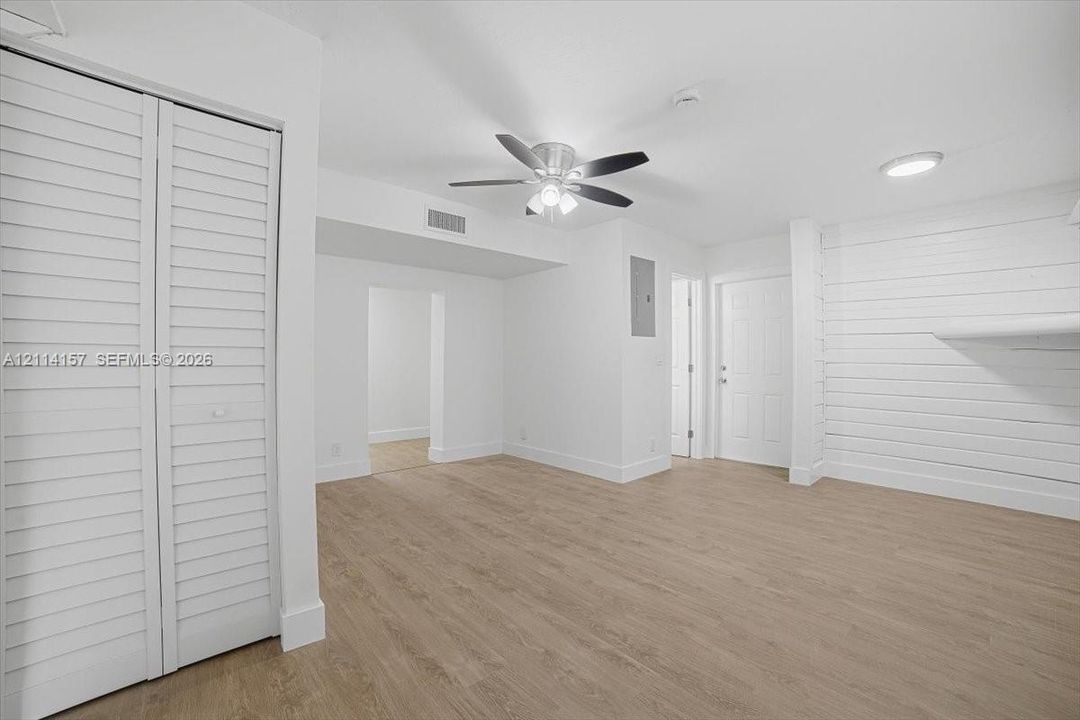 Interior space featuring wood-finish flooring, white shiplap accent wall, louvered bi-fold closet doors, and a ceiling fan with integrated lighting