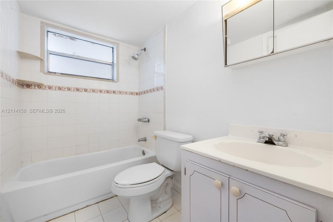 Full bathroom featuring a white tub-shower combination, tiled walls with decorative accents, built-in cabinetry vanity, and a recessed medicine cabinet