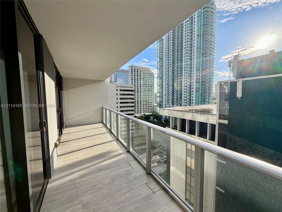 Covered balcony featuring wood-finish tile flooring, glass panel railings, and full-height sliding glass doors