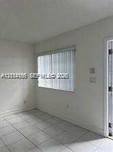Interior space featuring light-colored tile flooring, neutral walls, and a window fitted with vertical blinds