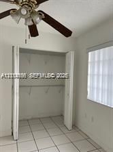 Ceramic tile flooring, ceiling fan with integrated lighting, reach-in closet with built-in shelving, and window with vertical blinds
