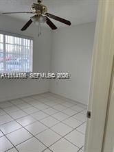 Neutral interior featuring white tile flooring, vertical blinds, and a multi-blade ceiling fan with integrated light fixture