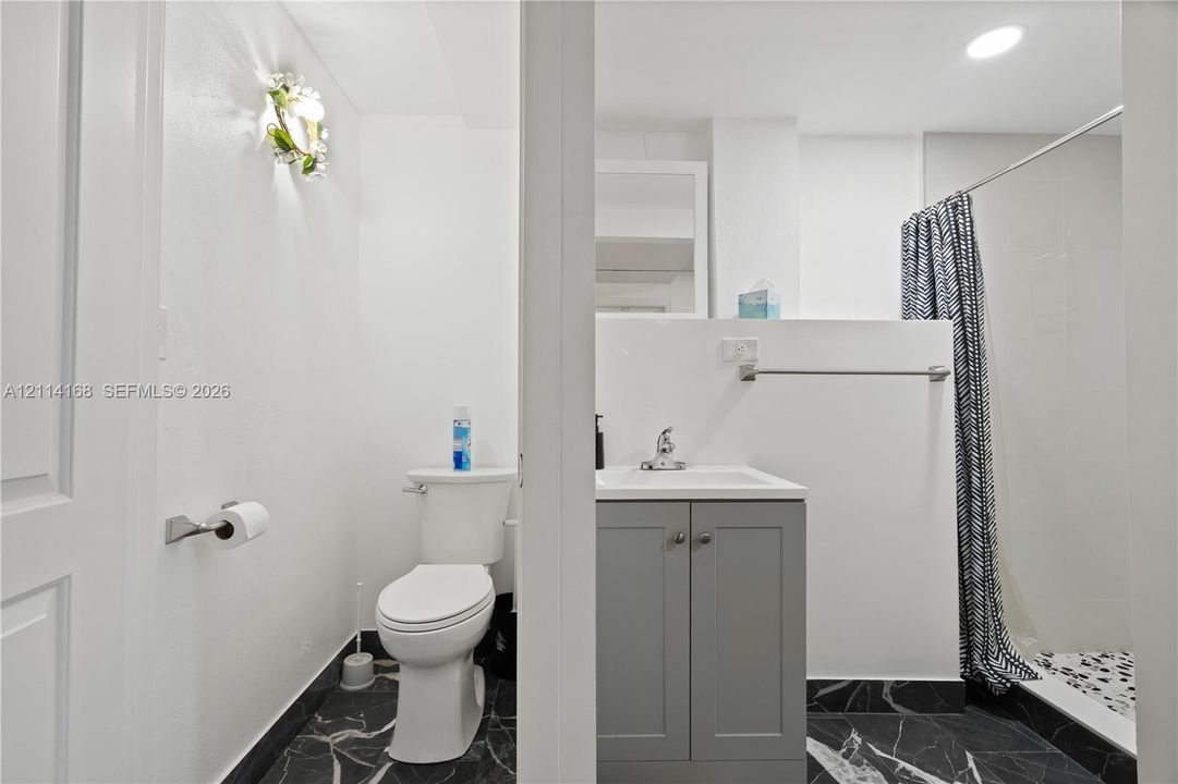 Bathroom featuring a grey vanity with a white countertop, chrome faucet, wall-mounted light fixture, and black veined stone-finish flooring. (Flex space, in-law quarters)
