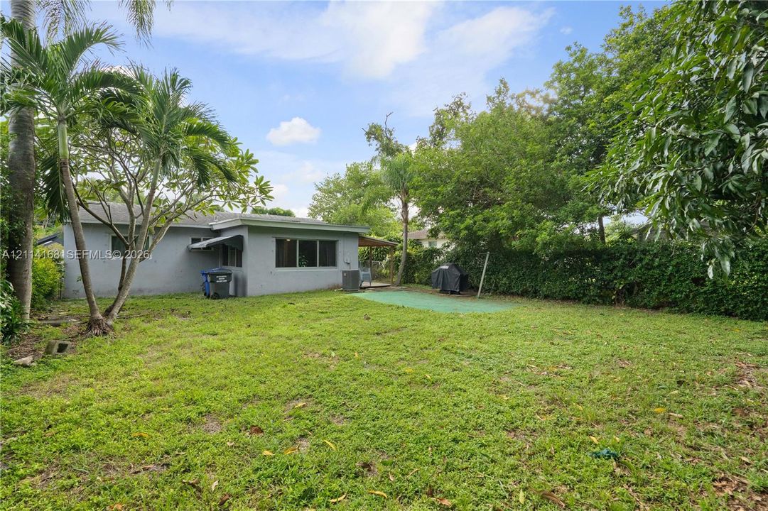 Expansive backyard featuring a large grass lawn, mature palm trees, perimeter landscaping, and a detached structure