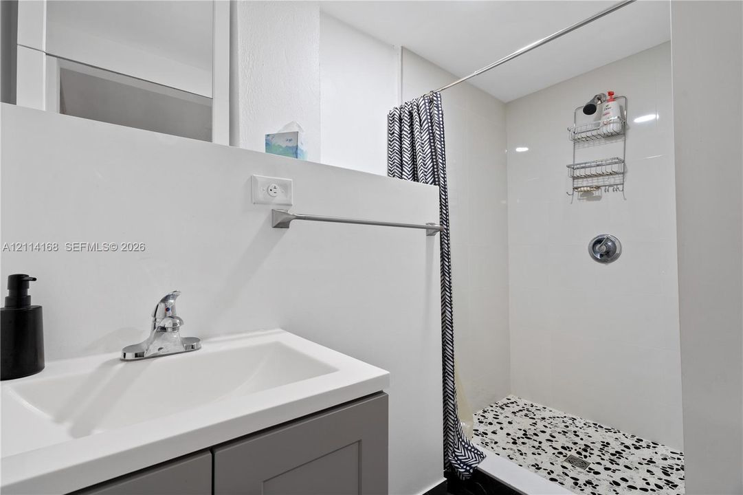 Bathroom featuring a gray vanity with a white countertop, polished chrome faucet, and a walk-in shower with white wall tile and a patterned floor (Flex space, in-law quarters)