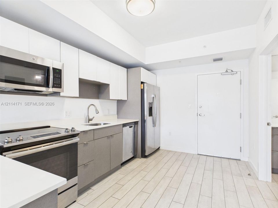 Kitchen featuring white upper cabinetry, grey lower cabinetry, stainless steel appliances, solid surface countertops, and wood-finish tile flooring