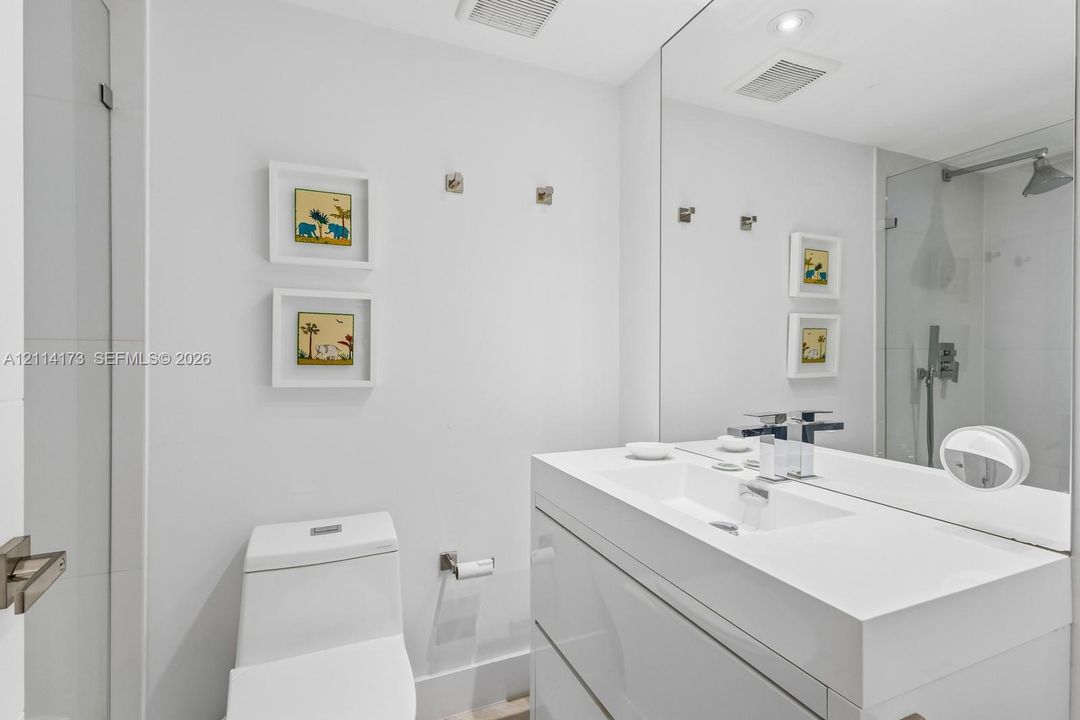Modern floating vanity with a seamless integrated sink, polished chrome widespread faucet, large-format mirror, and glass-enclosed shower featuring a wall-mounted rainfall showerhead