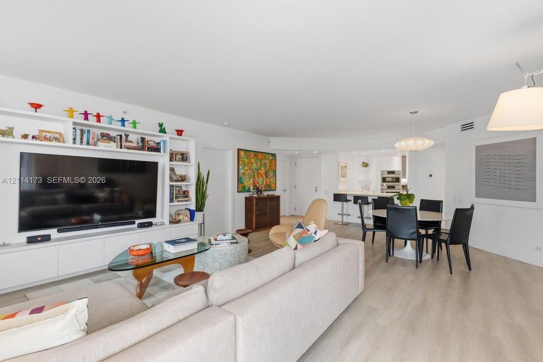 Open-concept floor plan featuring light wood-finish flooring, custom built-in cabinetry with integrated shelving, recessed lighting, and a kitchen island with stone countertop