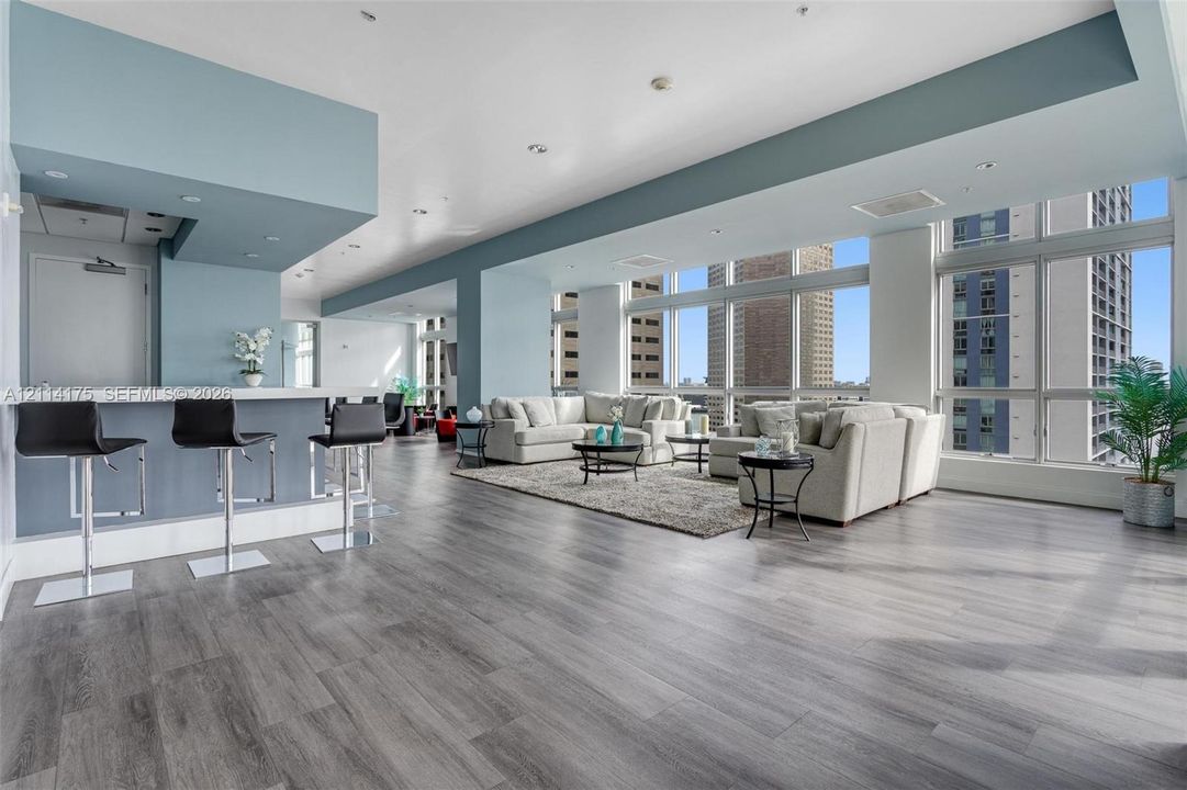 Open-concept living space featuring wood-finish flooring, floor-to-ceiling windows, recessed lighting, and a built-in wet bar with a countertop