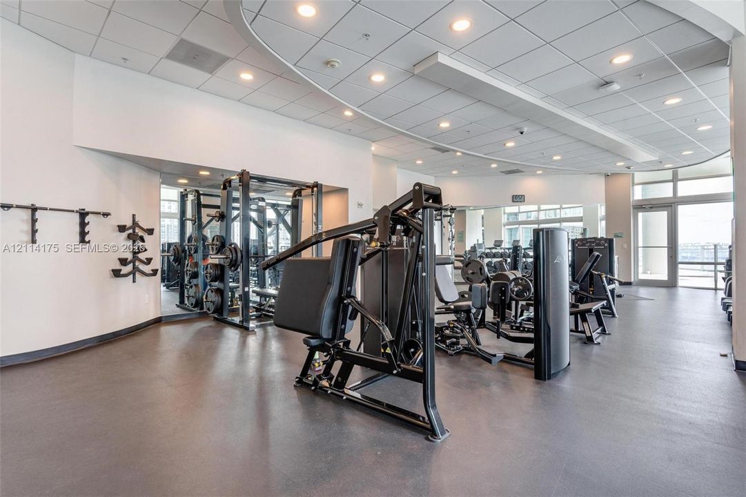 Fitness center featuring rubberized flooring, recessed ceiling lighting, wall-mounted weight storage, and expansive mirrors