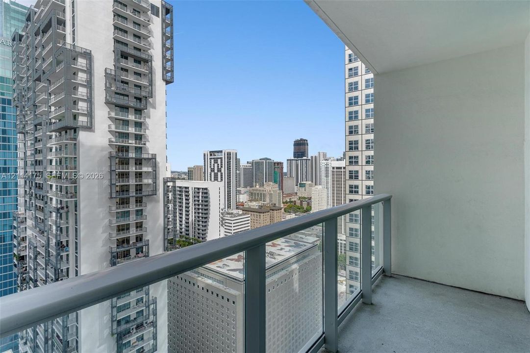 Private balcony featuring glass and metal railing with urban high-rise surroundings