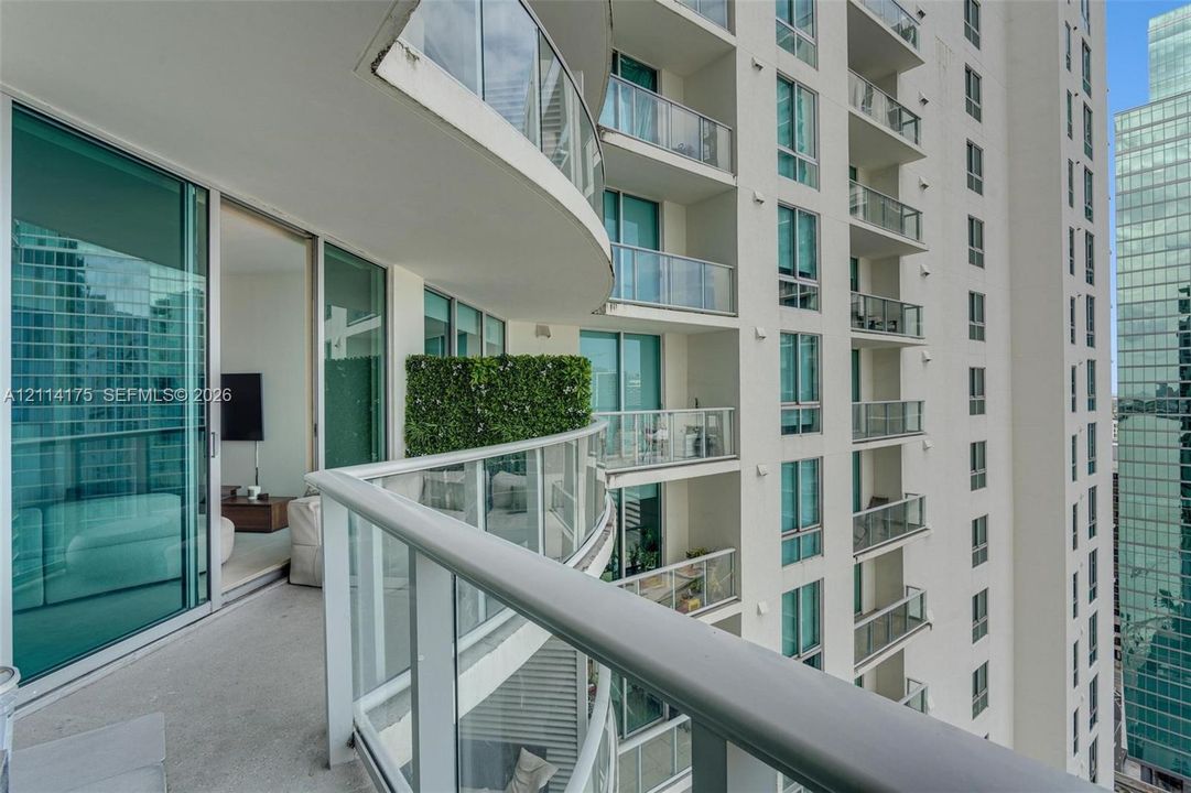 Curved balcony featuring glass panel railings, floor-to-ceiling sliding glass doors, and concrete flooring