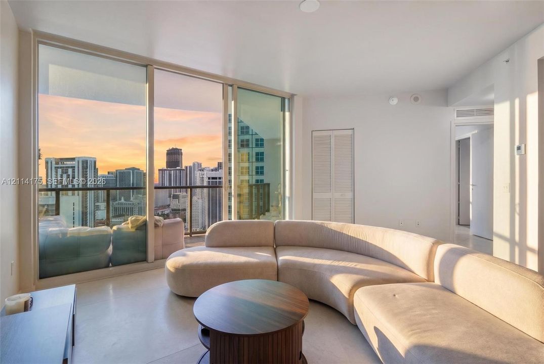 Floor-to-ceiling windows, private balcony with metal railing, urban skyline scenery, and crisp neutral wall finishes