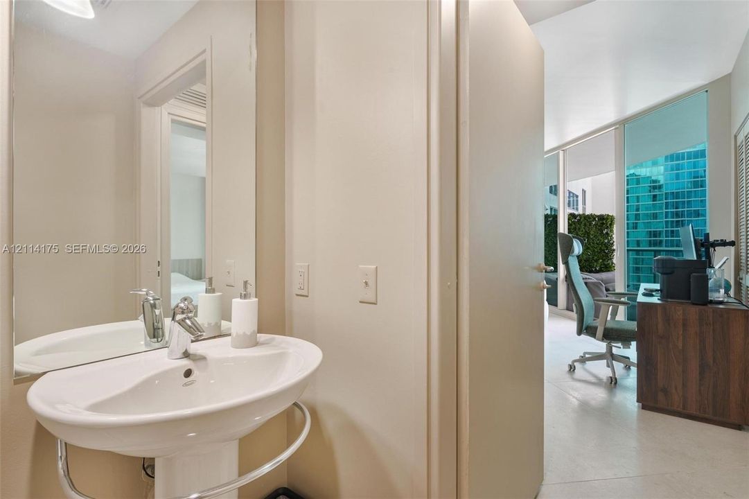 Wall-mounted pedestal sink with chrome faucet and integrated towel rail, accompanied by a large frameless mirror and stone-finish flooring