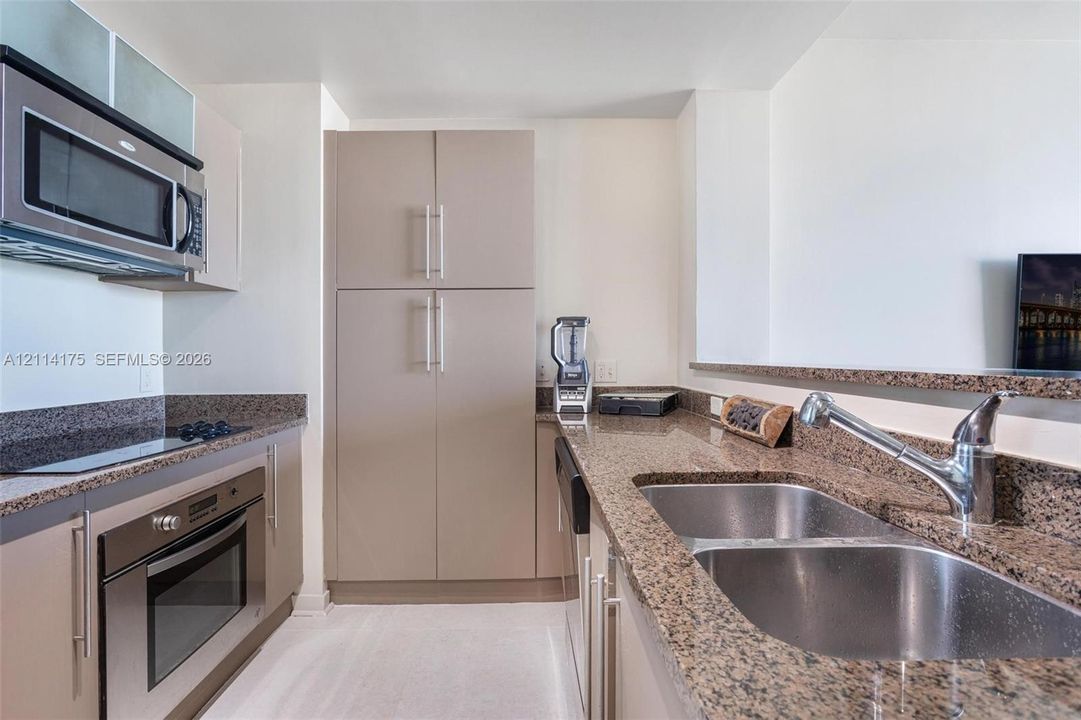 Kitchen featuring speckled stone countertops, stainless steel dual-basin undermount sink with a high-arch pull-down faucet, integrated stainless steel oven, built-in microwave, and flat-panel cabinetry