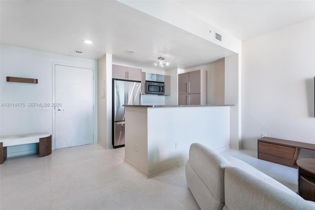 Kitchen area featuring stainless steel refrigerator, microwave, flat-panel cabinetry, and a stone-topped peninsula